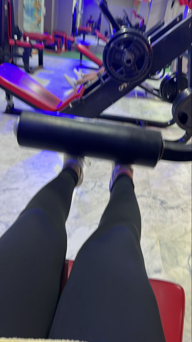 the legs of a person sitting on a bench in front of a gym equipment machine