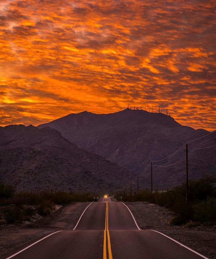 an empty road in the desert with mountains in the background at sunset or sunrise time