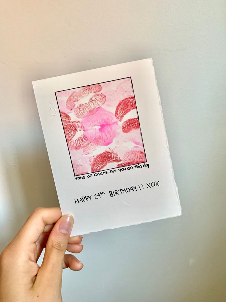 a person holding up a birthday card in front of a white wall with pink flowers on it