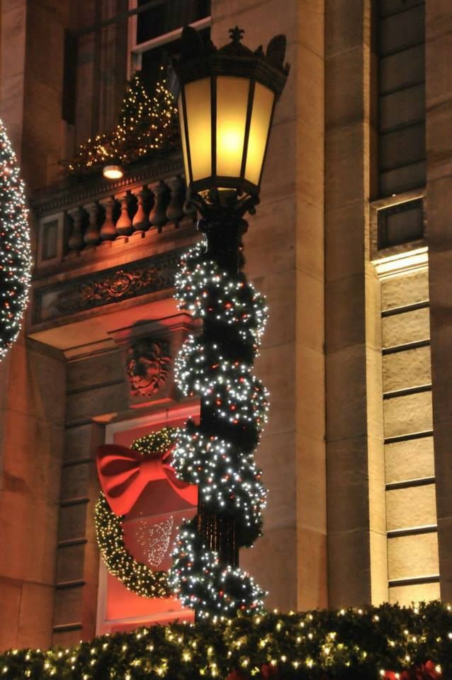 a street light decorated with christmas lights and wreaths in front of a large building