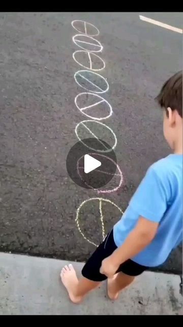 a little boy standing on the sidewalk with his feet in the air and chalk writing