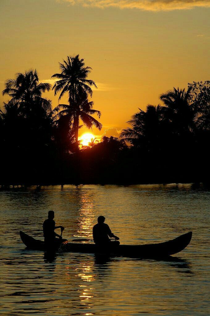 two people are in a canoe on the water at sunset with palm trees behind them