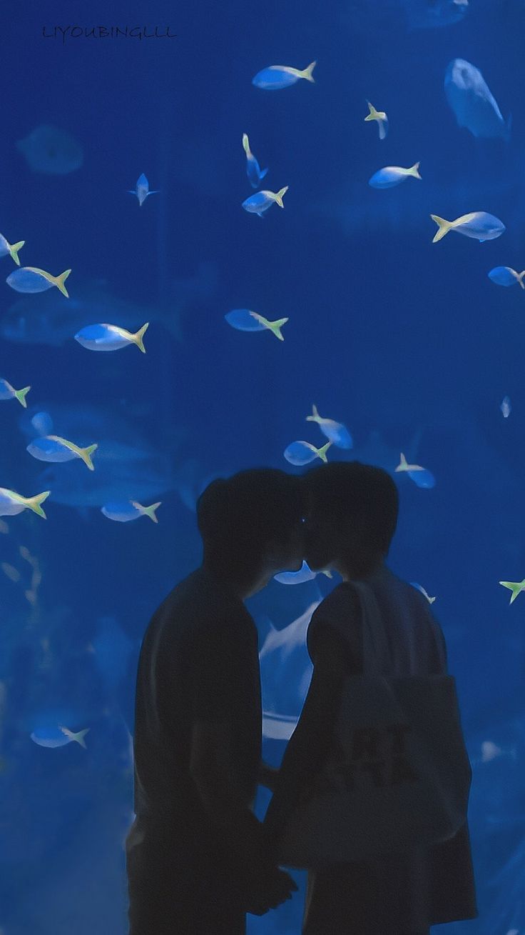 two people kissing in front of a large aquarium with fish on the wall behind them