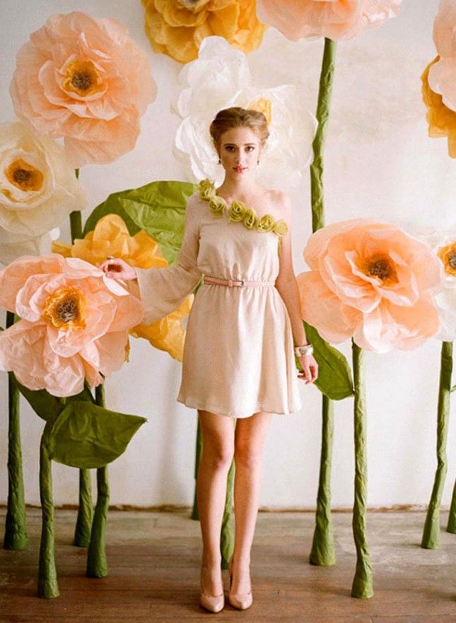 a woman standing in front of giant paper flowers with leaves and petals around her body