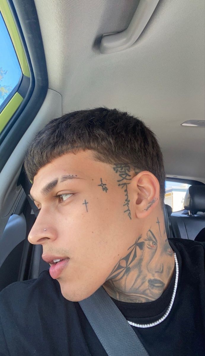 a man with tattoos on his face sitting in a car