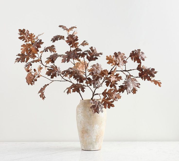 a vase filled with lots of leaves on top of a white table next to a wall