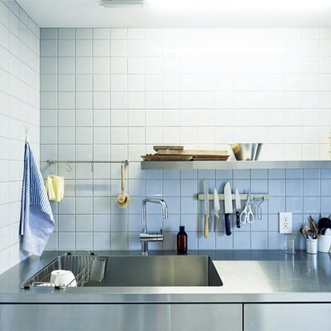 a stainless steel sink in a kitchen with blue tiles on the wall and shelves above it