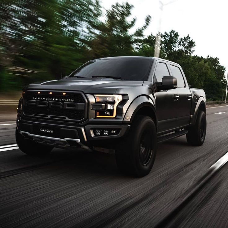 a black truck driving down the road with trees in the background