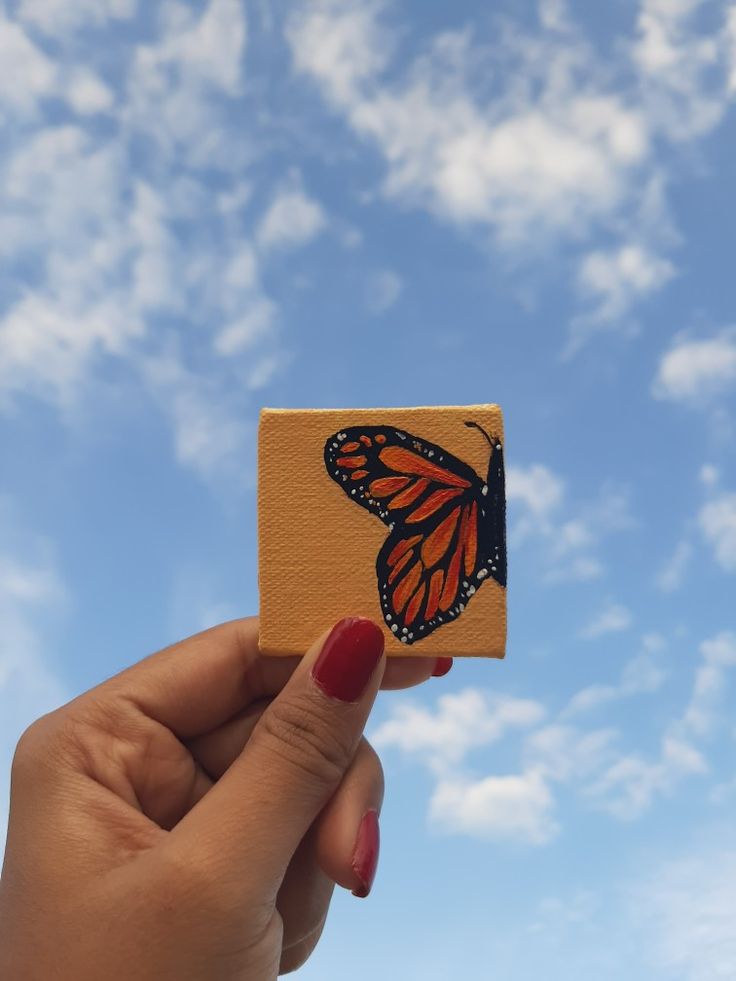 a hand holding up a small wooden block with a butterfly painted on it's side