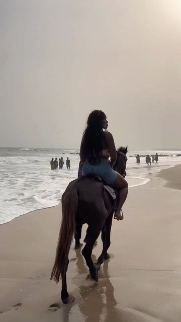 a woman riding on the back of a brown horse down a beach next to the ocean