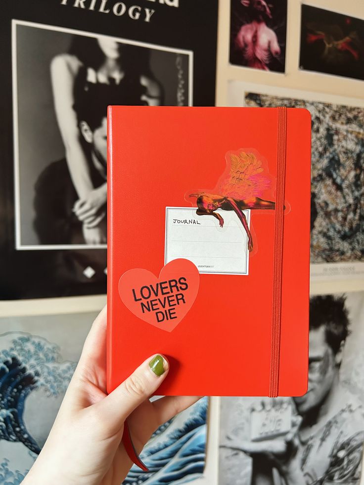 a person holding up a red book with stickers on it that says lovers never die