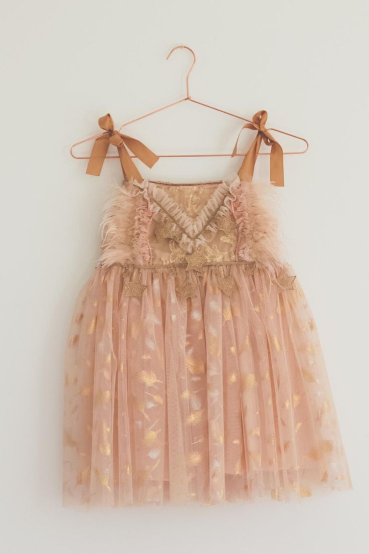 This golden peach tutu dress is the perfect addition to your little ones wardrobe One of a kind design The skirt is crafted from multiple layers of soft peach tulle, creating volume and the top layer features a gold feather design that creates a dreamy effect, perfect for twirling and dancing! The bodice is constructed from sparkly sequin fabric and delicately adorned with ruffled tulle, peach feathers and gold star trim The gold satin ribbon ties ensure a customisable fit, making it easy to adj Girls Tulle Dress, Gold Feathers, Special Occasion Dress, Gold Satin, Feather Design, Sequin Fabric, Gold Star, Ribbon Tie