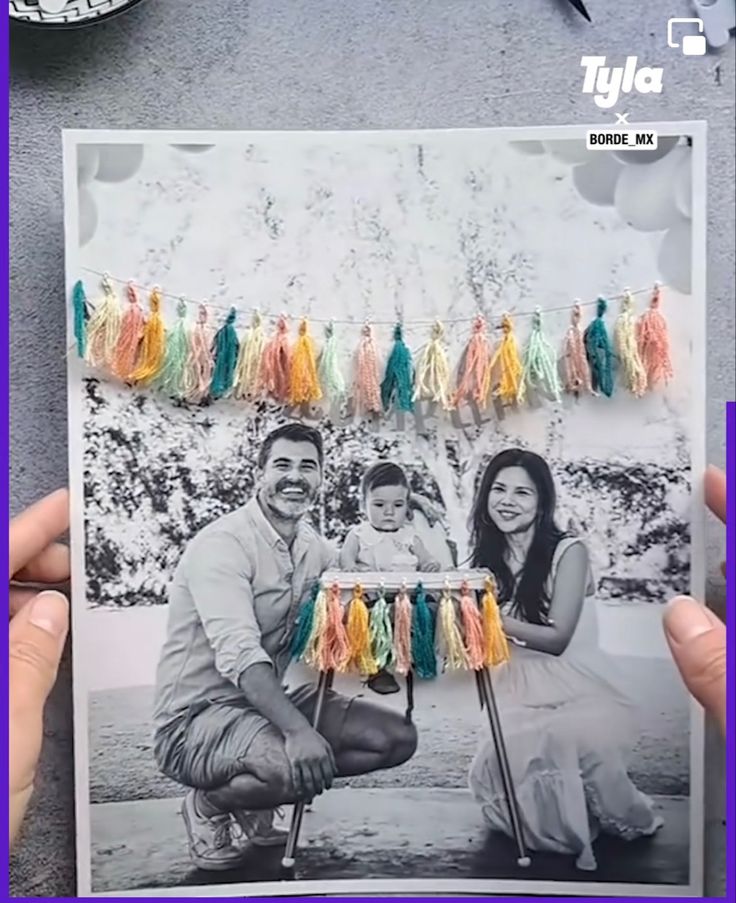 a man and woman holding up a photo with tassels hanging from it