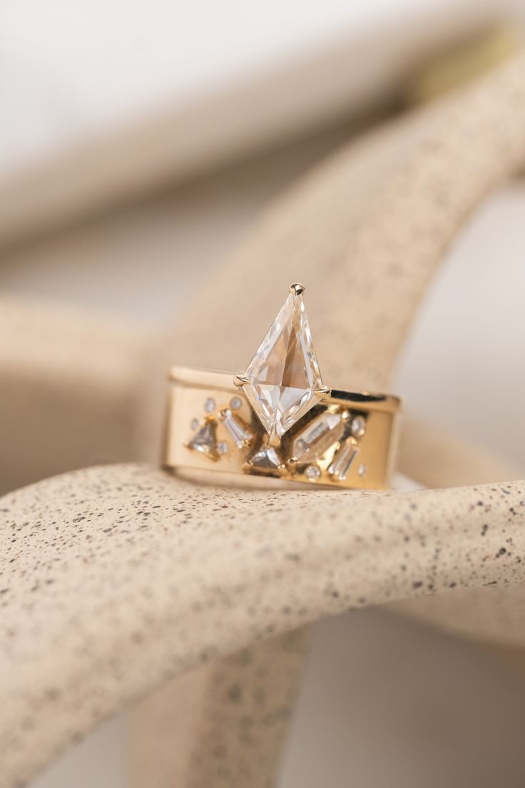 a diamond ring sitting on top of a white piece of wood with other items in the background