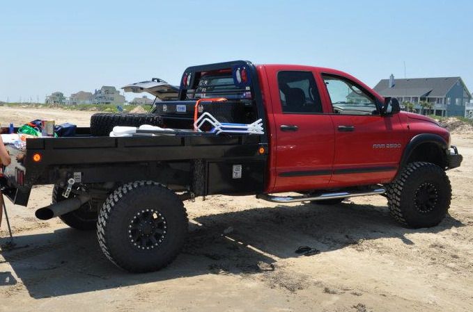 a man sitting in the back of a red truck on top of a sandy beach