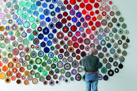 a man standing in front of a wall made out of different colored circles on it