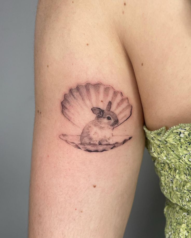 a woman's arm with a small tattoo of a mouse in a shell