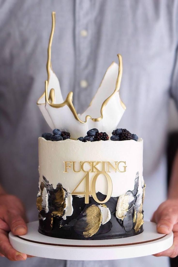 a man holding a cake with white frosting and gold leaf decorations on the top