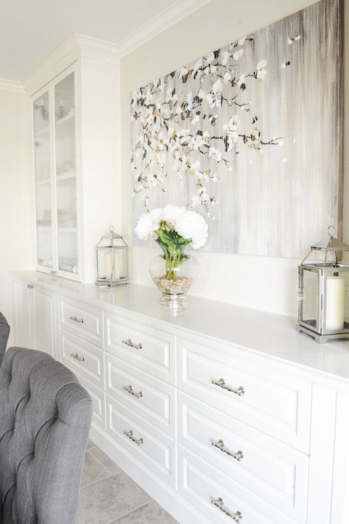 a white dresser with flowers in a vase on top and a gray chair next to it