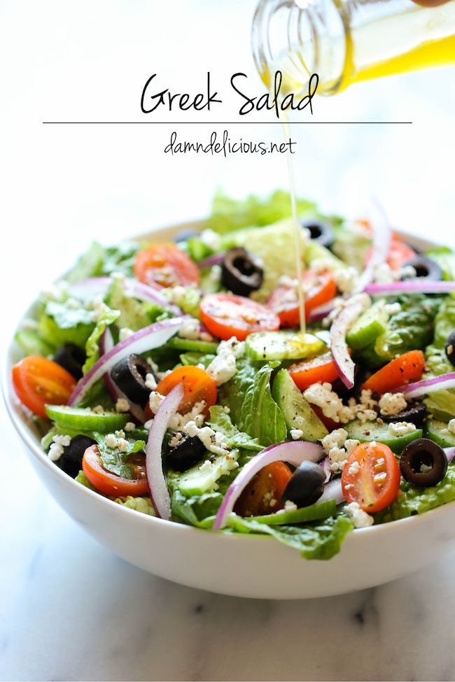 a salad with olives, tomatoes, lettuce and other vegetables being drizzled with dressing