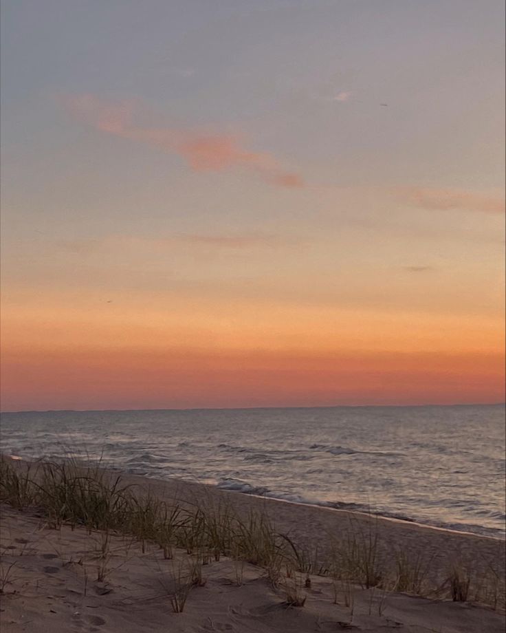 a bench sitting on top of a sandy beach next to the ocean at sunset or dawn