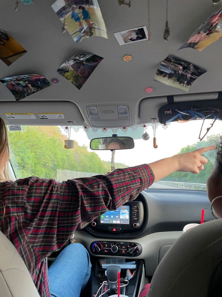 two people in the back seat of a car pointing at pictures hanging from the ceiling