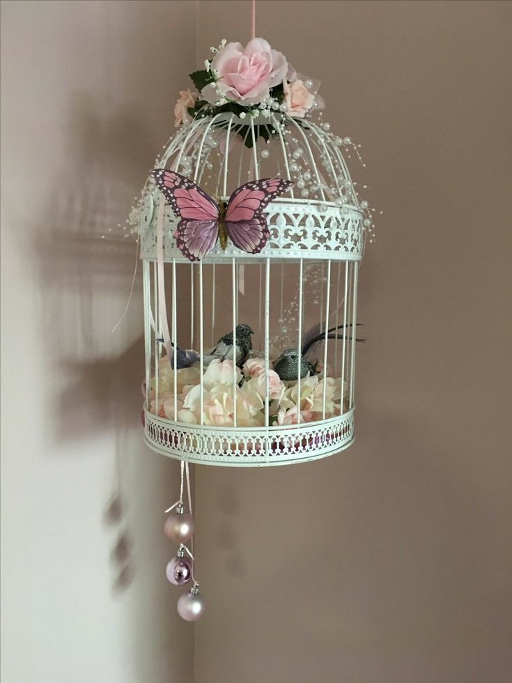 a white birdcage with pink flowers and butterflies hanging from it's sides