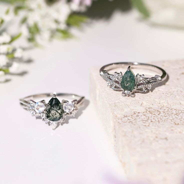 two engagement rings sitting on top of a rock next to some flowers and greenery