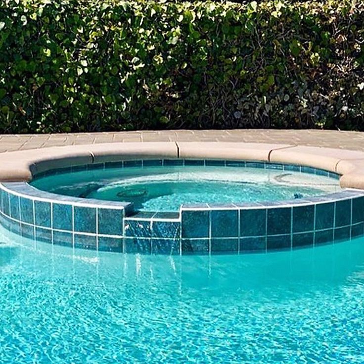 an outdoor swimming pool with blue tiles on the sides and green bushes in the background