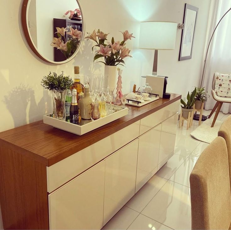 a white dresser topped with lots of bottles and vases next to a mirror on the wall