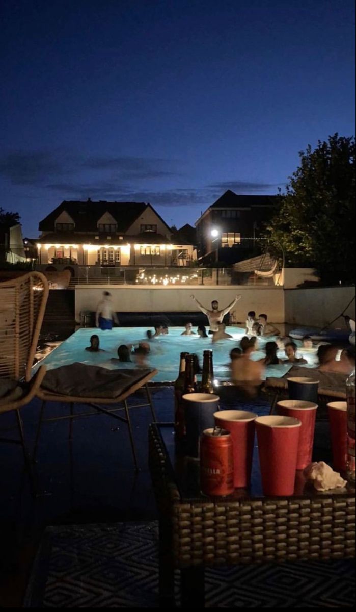 an outdoor swimming pool at night with people in the water and buckets full of drinks