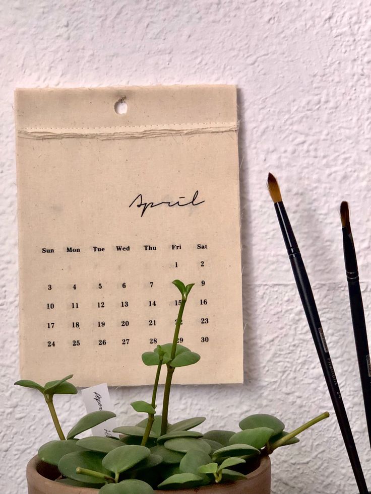 a calendar is hanging on the wall above a potted plant with two brushes next to it