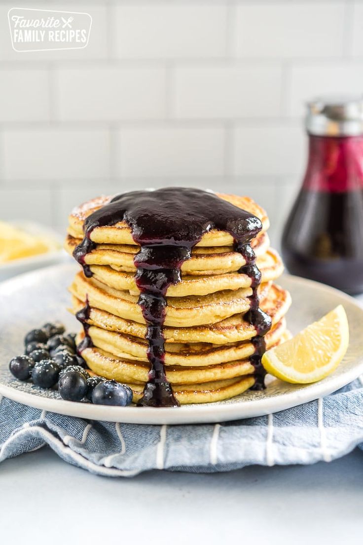 stack of blueberry syrup pancakes on a white plate with lemon wedges and blueberries