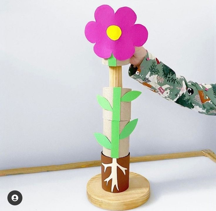 a young child is playing with a flower made out of construction paper and wood sticks