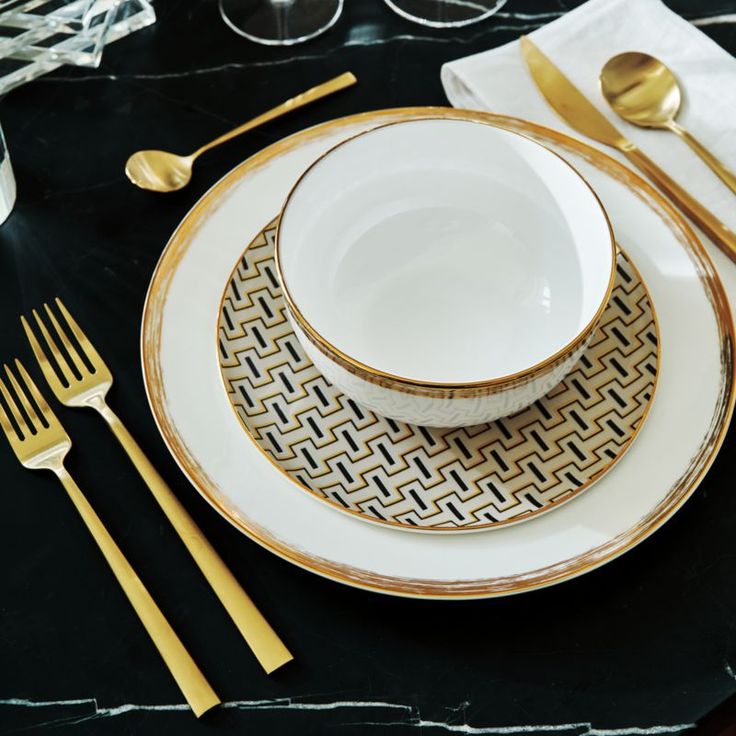 a white and gold dinner set with silverware on a black marble tableclothed place setting