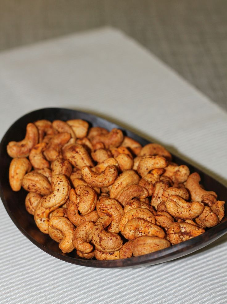 a black bowl filled with cashews on top of a white table cloth next to a wooden spoon