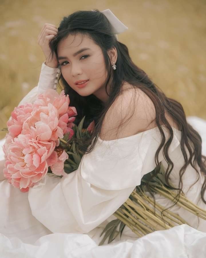 a woman in a white dress holding a bouquet of flowers and wearing a bow on her head