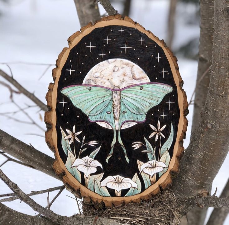 a painted wooden sign on a tree in the snow with white flowers and a full moon behind it