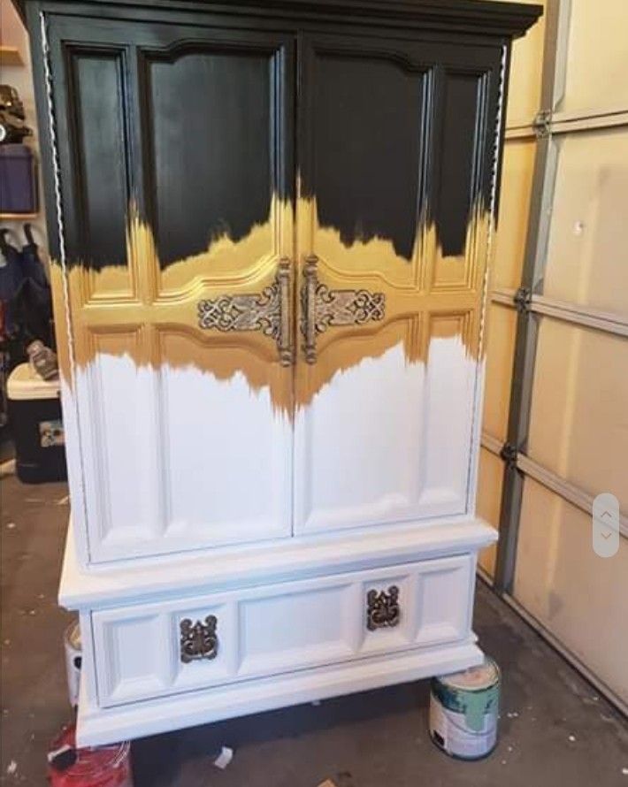 an armoire painted black and white with gold paint on the top, in a garage