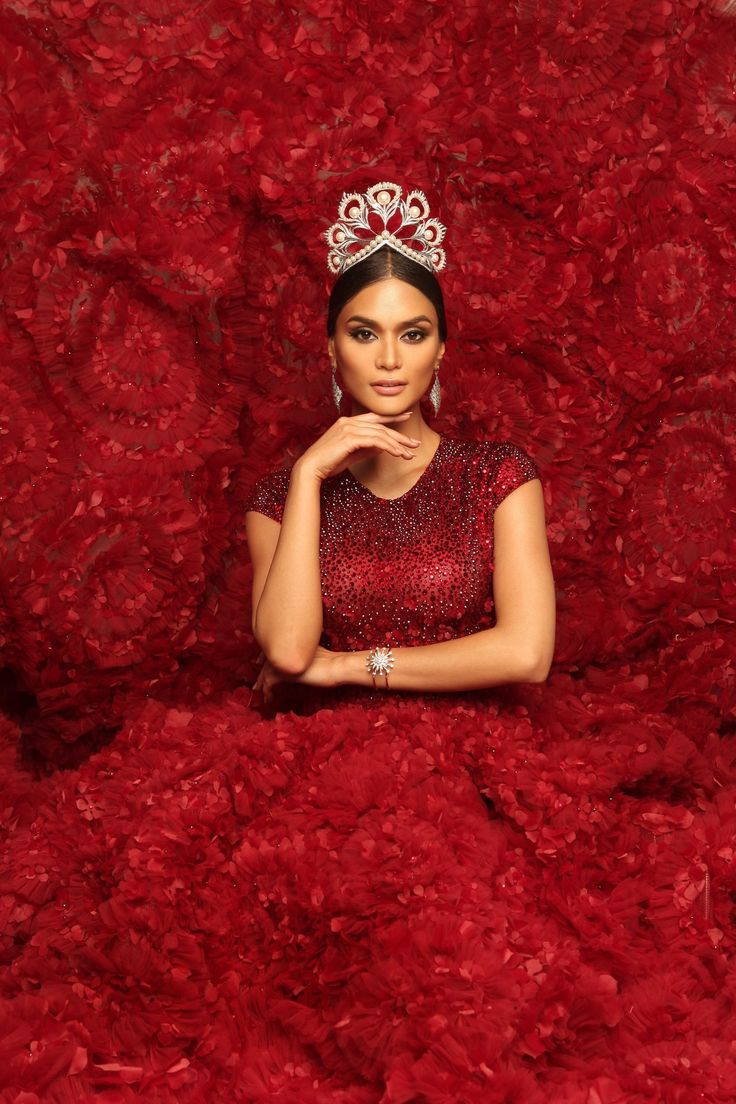 a woman wearing a tiara sitting on top of a pile of red fur with her hand under her chin