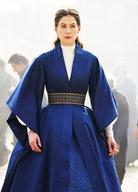 a woman in blue dress standing on street next to other people and looking at camera