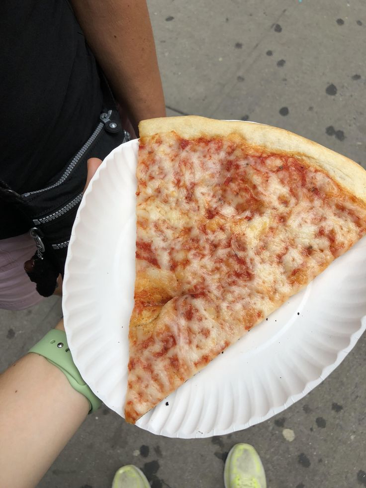 a slice of pizza on a paper plate being held by a person's hand