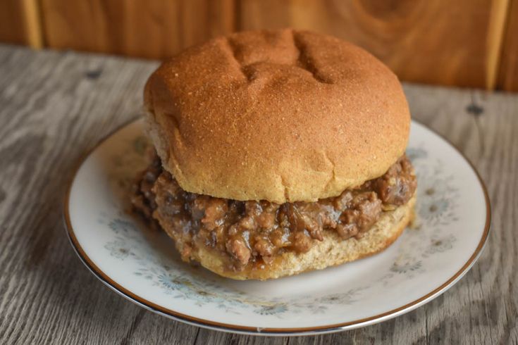 a hamburger sitting on top of a white plate next to a wooden wall and table