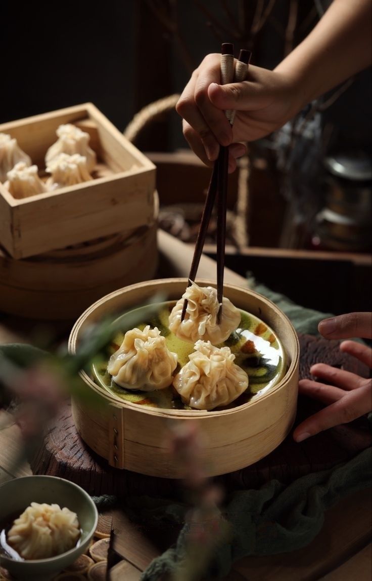 a person holding chopsticks above a bowl of dumplings