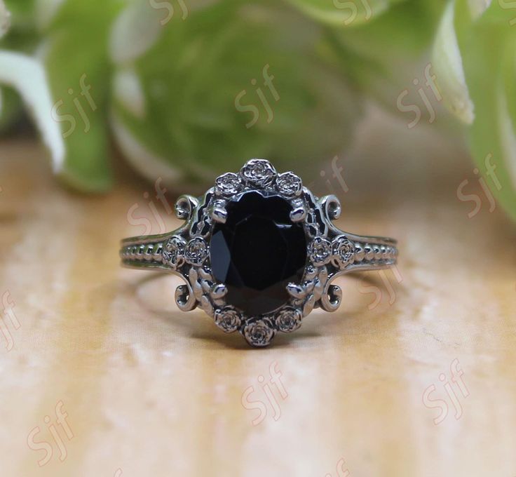 a black diamond ring sitting on top of a wooden table next to green leaves and flowers