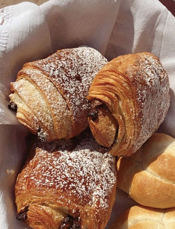 three croissants sitting in a basket with powdered sugar on top, and two pastries next to each other