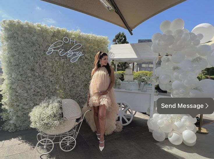 a woman in a dress is sitting next to a baby carriage and balloon arch with the words send message on it