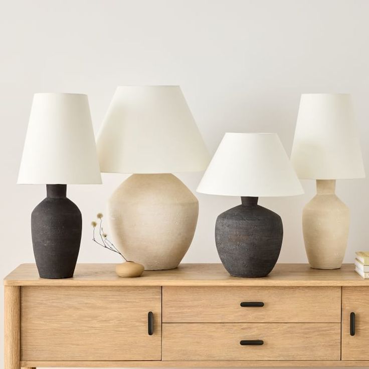 three vases with lamps sitting on top of a wooden dresser next to each other