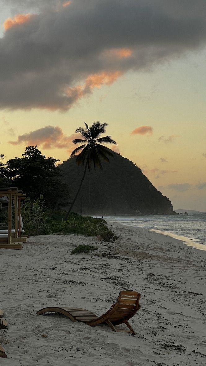 two lounge chairs sitting on top of a sandy beach next to the ocean under a cloudy sky