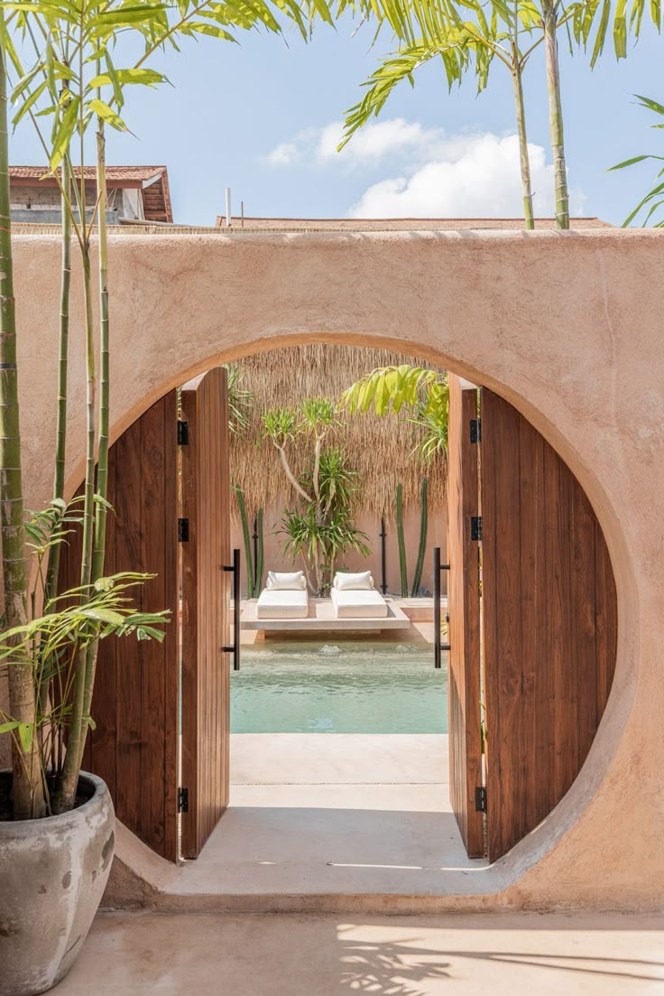 an entrance to a pool with palm trees in the foreground and a walkway leading into it